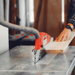 A man carves a tree. The carpenter works with saw in a studio. An engineer provides a tree shape